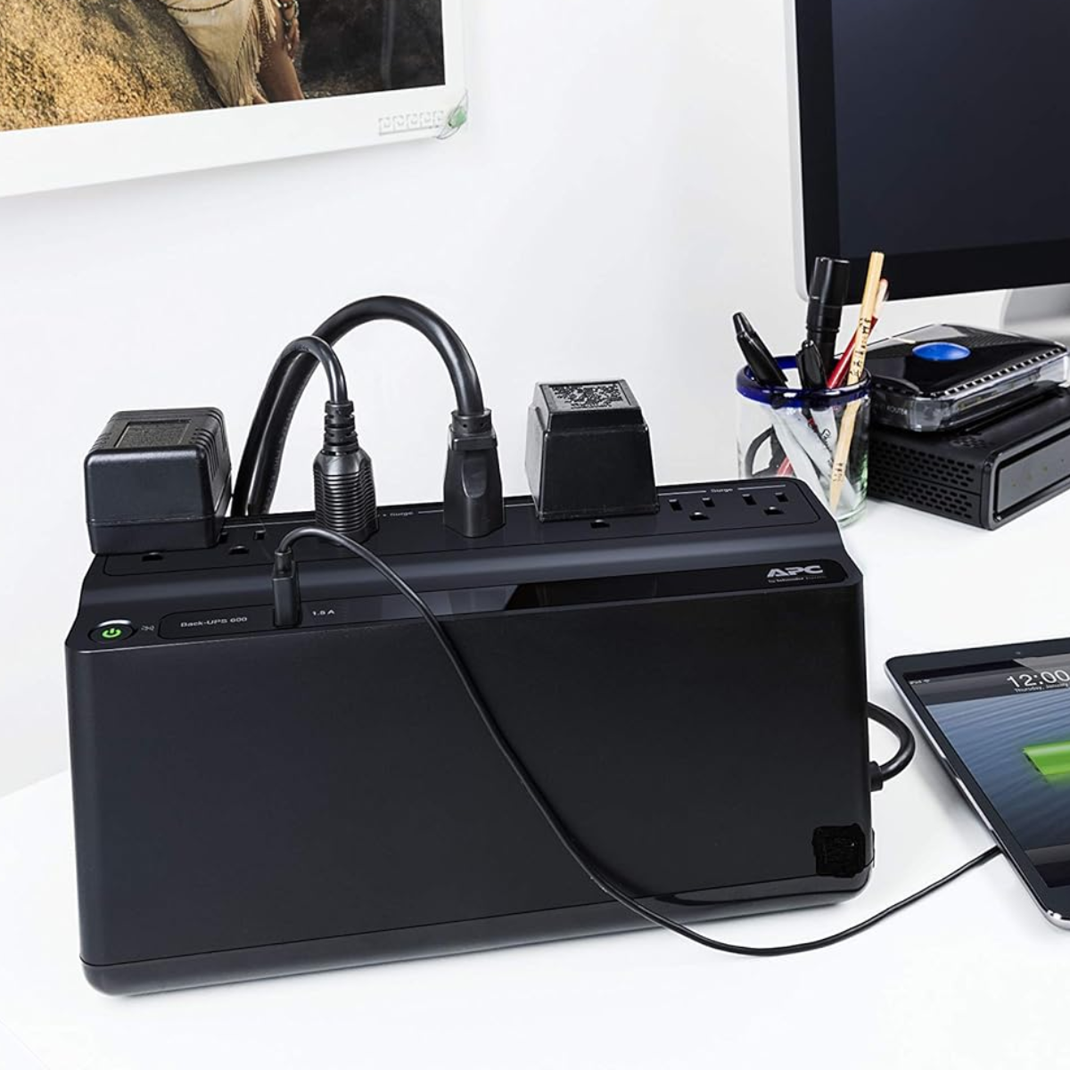 APC UPS Battery Backup &amp; Surge Protector on a desktop with an iPad, computer, and other electronics plugged in.