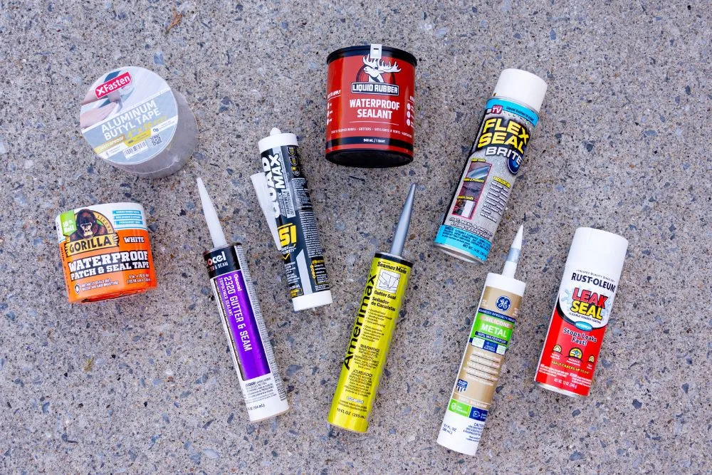 Найкращі герметики для жолобів 2026: експертний тест 30 Nine gutter sealants, tapes, and caulks laying on a granite countertop